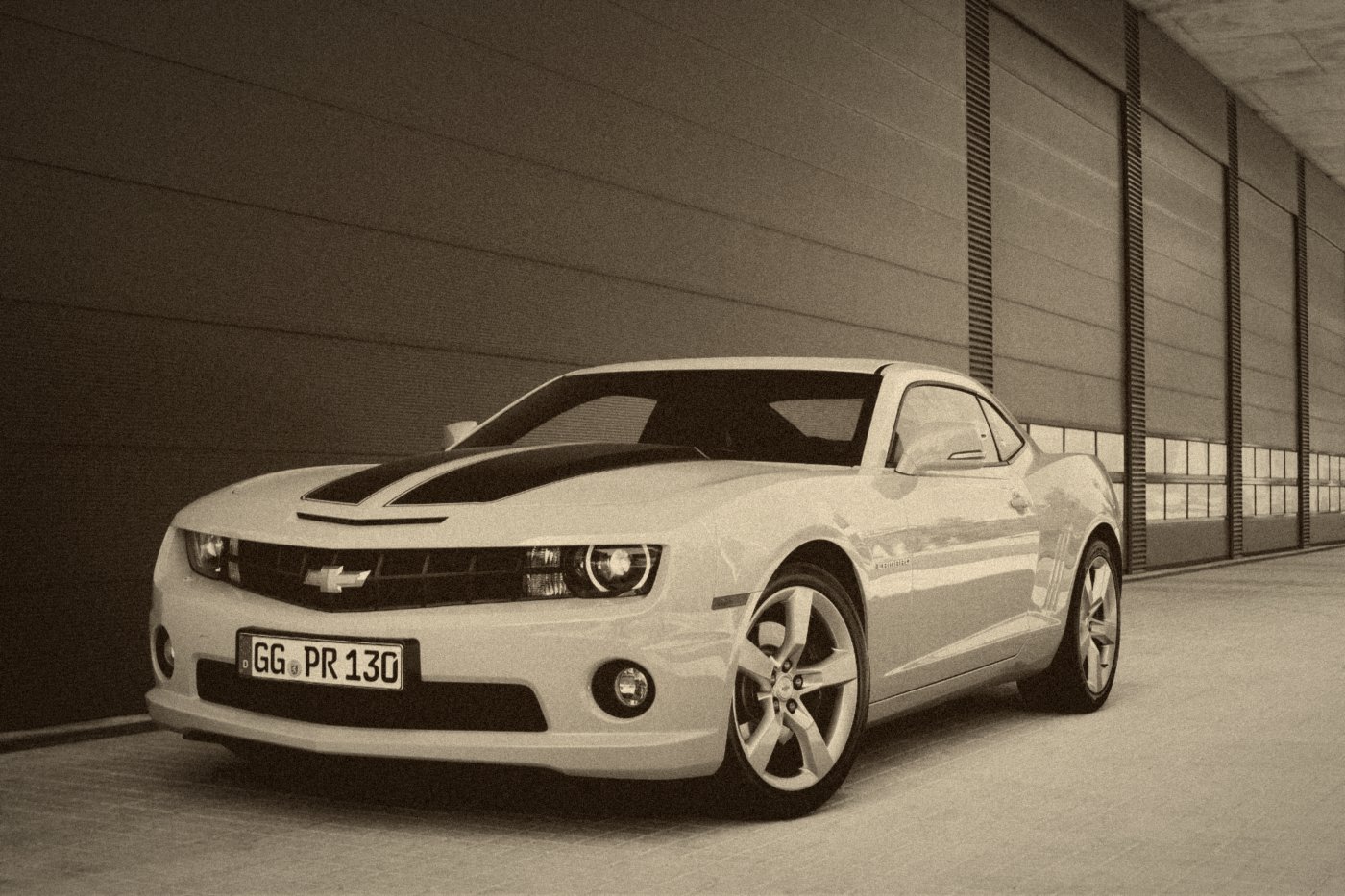 Chevrolet Camaro jaune à bandes noires, style Bumblebee, devant un mur rouge