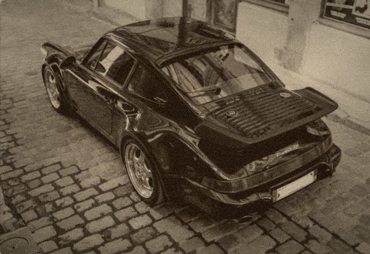 Porsche 911 Turbo (964) bleu nuit, vue de trois-quarts arrière surélevée, sur une rue pavée
